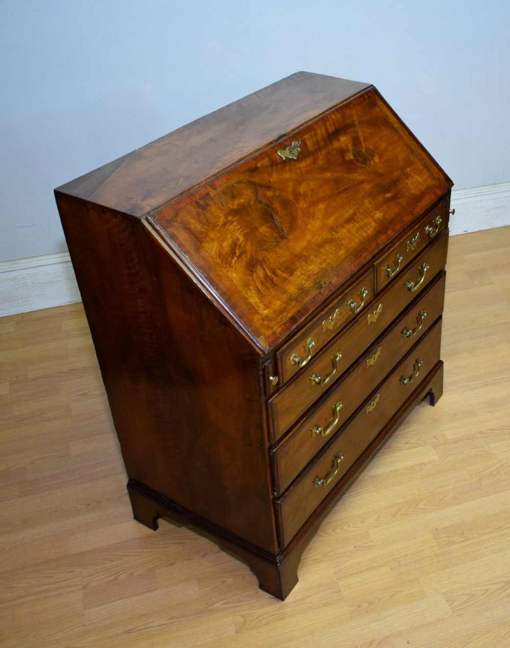 A Georgian walnut bureau featuring a sloped hinged front opening above four graduated drawers with decorative brass handles and bracket feet. View VIII