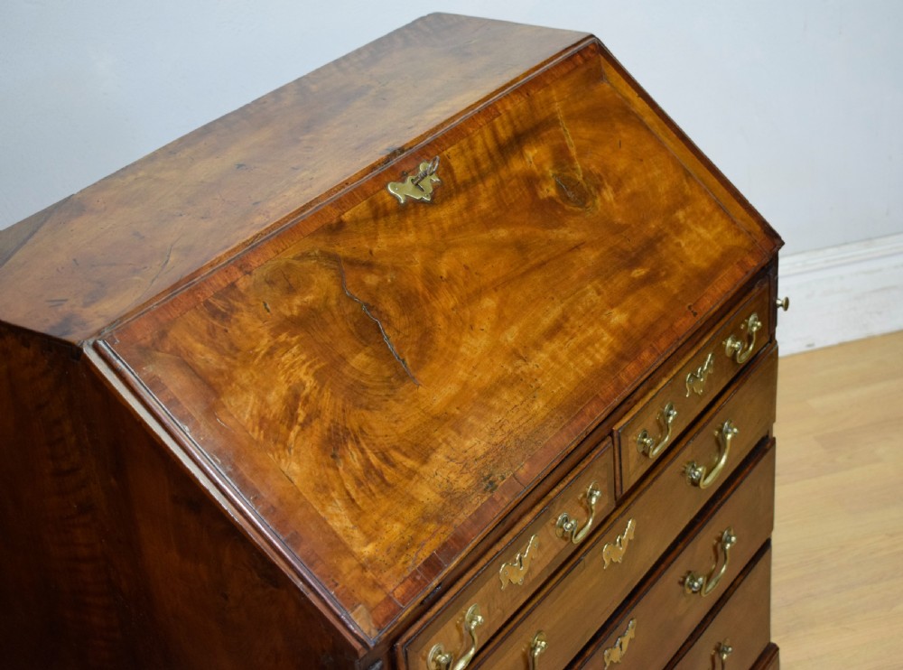A Georgian walnut bureau featuring a sloped hinged front opening above four graduated drawers with decorative brass handles and bracket feet. View IX