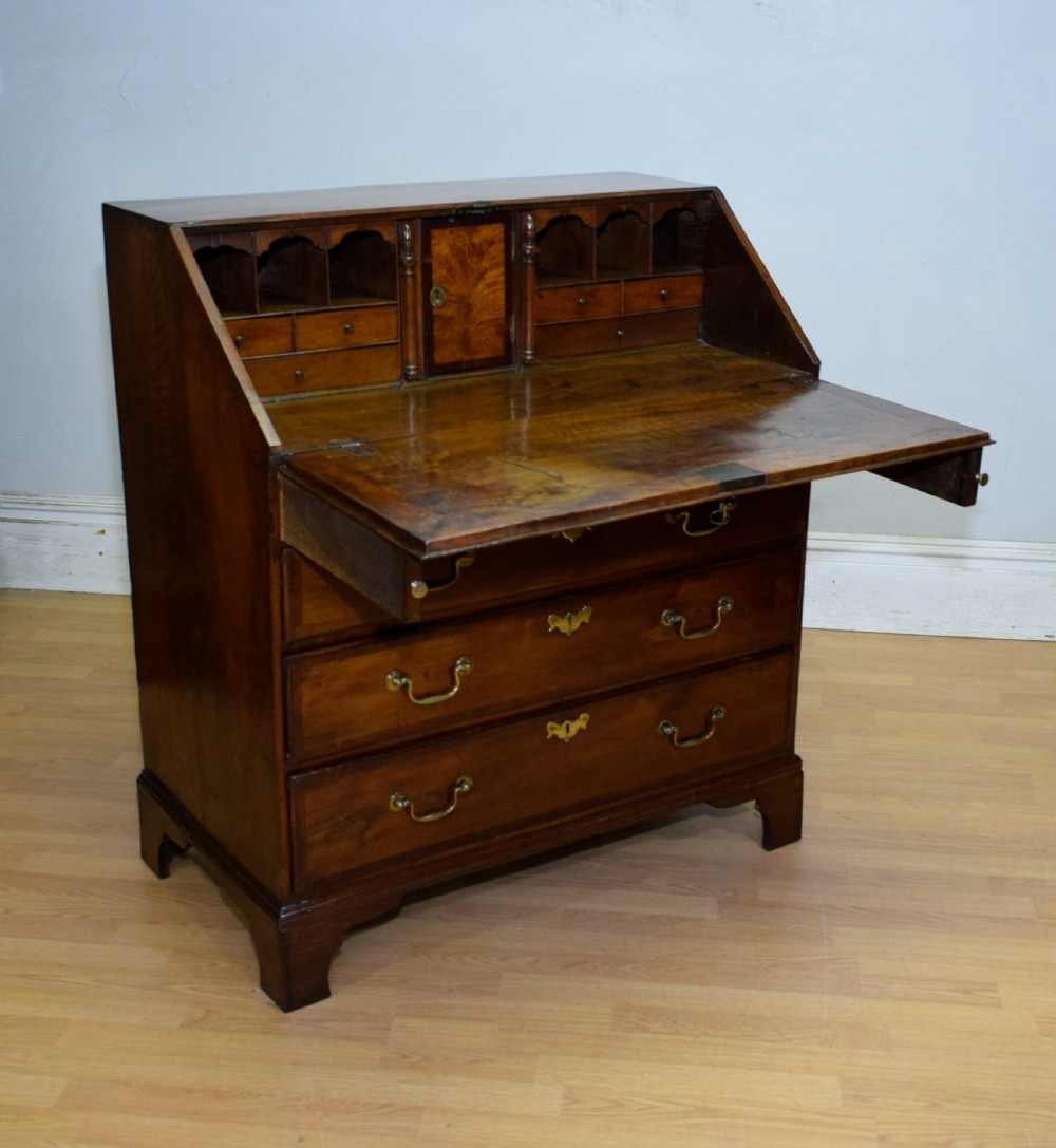 A Georgian walnut bureau featuring a sloped hinged front opening above four graduated drawers with decorative brass handles and bracket feet. View XII