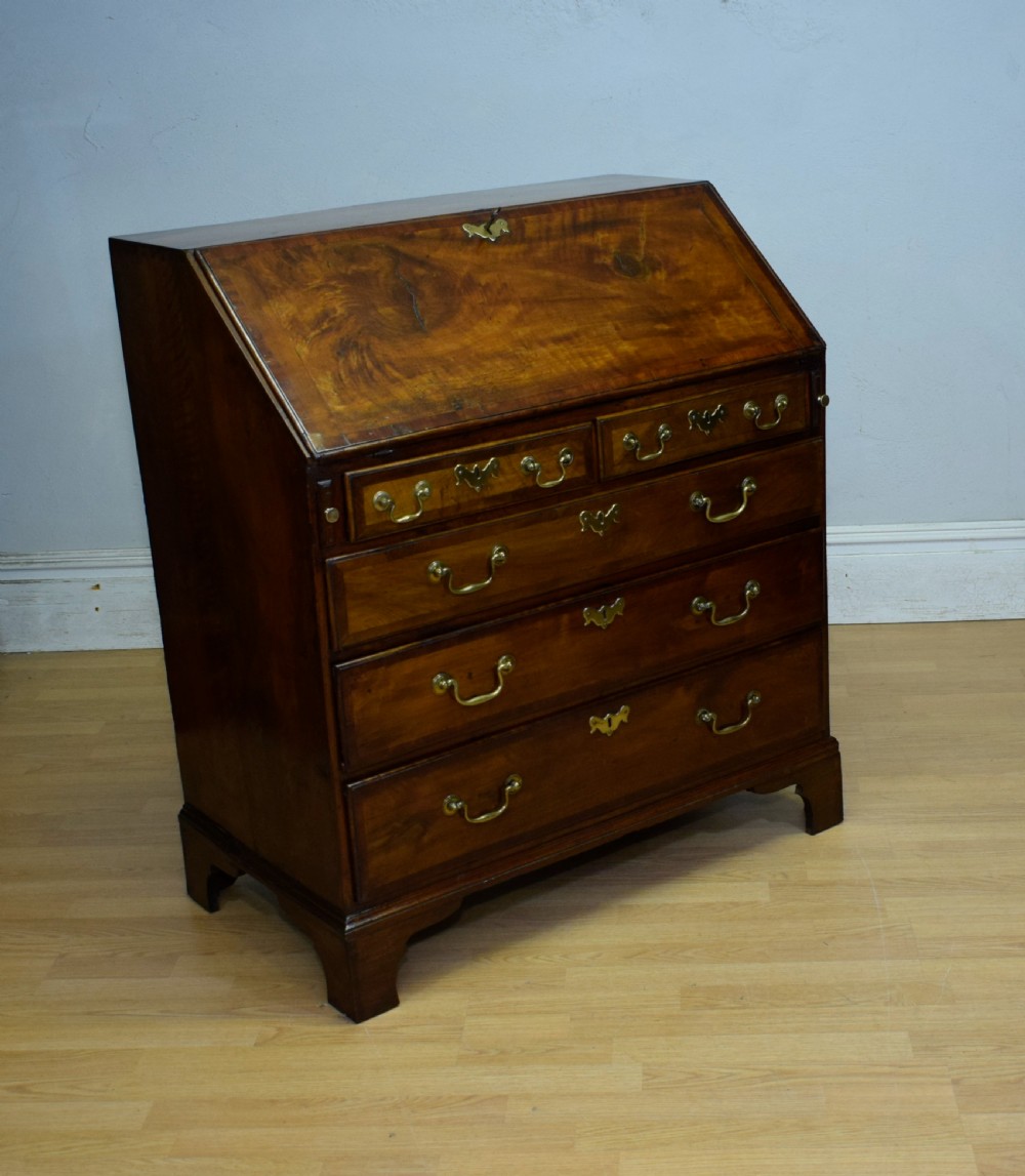 A Georgian walnut bureau featuring a sloped hinged front opening above four graduated drawers with decorative brass handles and bracket feet. View XIX