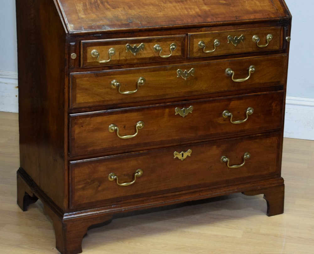 A Georgian walnut bureau featuring a sloped hinged front opening above four graduated drawers with decorative brass handles and bracket feet. View XX