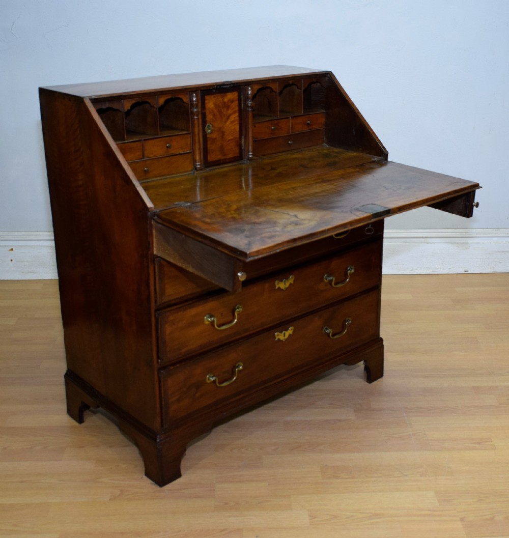 A Georgian walnut bureau featuring a sloped hinged front opening above four graduated drawers with decorative brass handles and bracket feet. View XXI