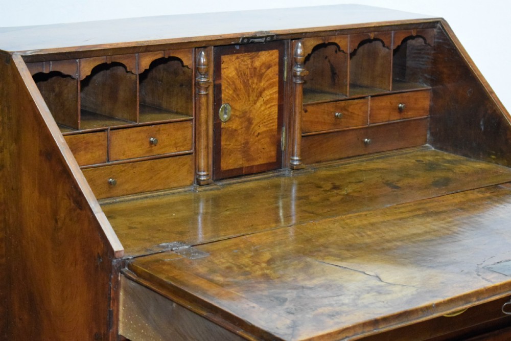 A Georgian walnut bureau featuring a sloped hinged front opening above four graduated drawers with decorative brass handles and bracket feet. View XXII