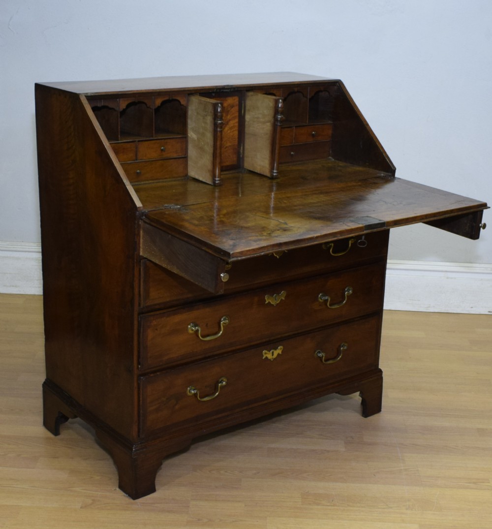 A Georgian walnut bureau featuring a sloped hinged front opening above four graduated drawers with decorative brass handles and bracket feet. View XXIII