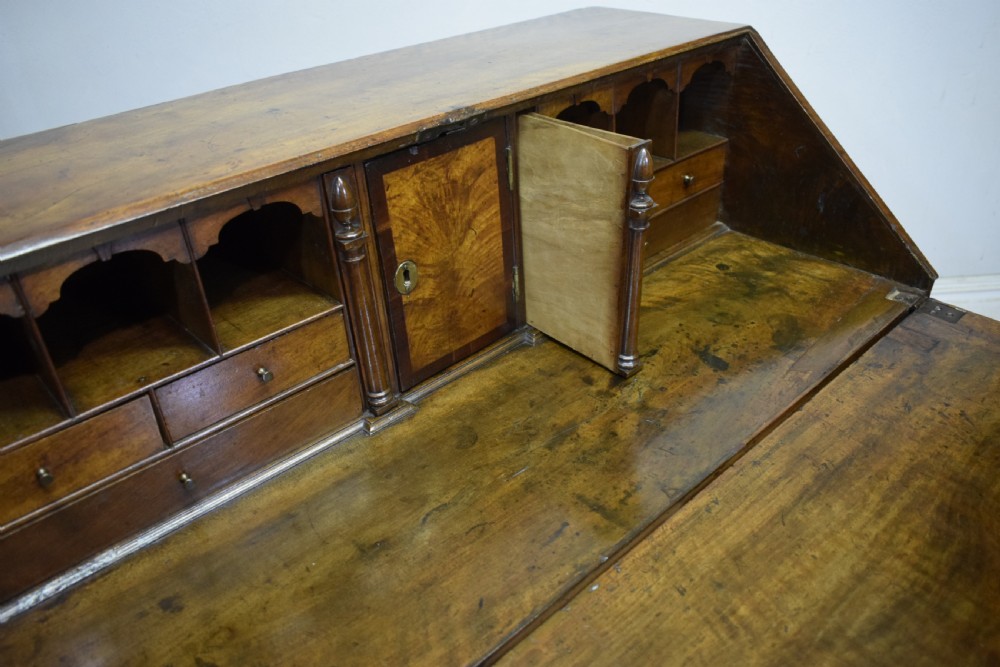 A Georgian walnut bureau featuring a sloped hinged front opening above four graduated drawers with decorative brass handles and bracket feet. View XXIV
