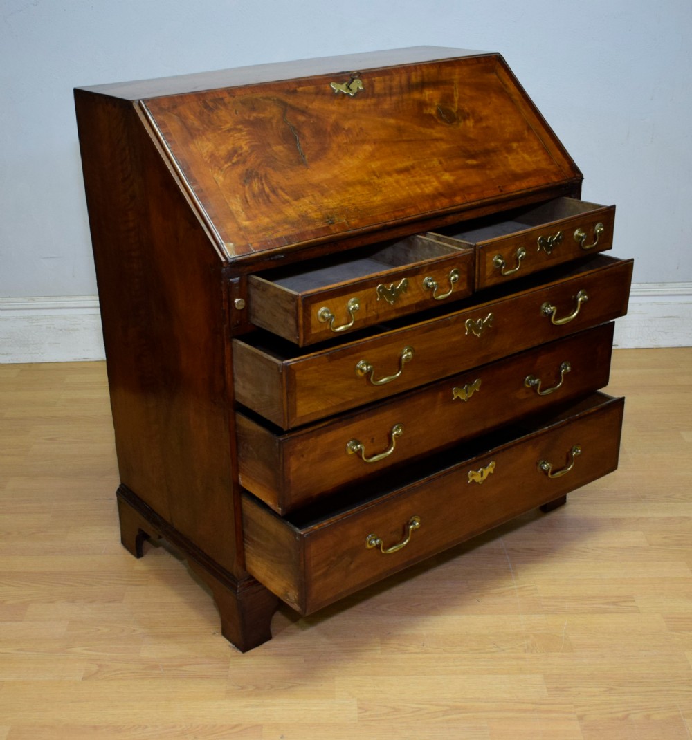 A Georgian walnut bureau featuring a sloped hinged front opening above four graduated drawers with decorative brass handles and bracket feet. View XXVIII