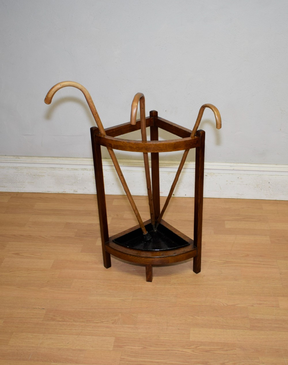An Arts and Crafts dark oak corner stick stand featuring a curved upper front rail, straight vertical supports, and a black triangular metal drip tray. View II