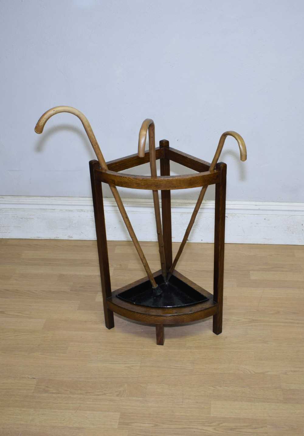 An Arts and Crafts dark oak corner stick stand featuring a curved upper front rail, straight vertical supports, and a black triangular metal drip tray. View IV
