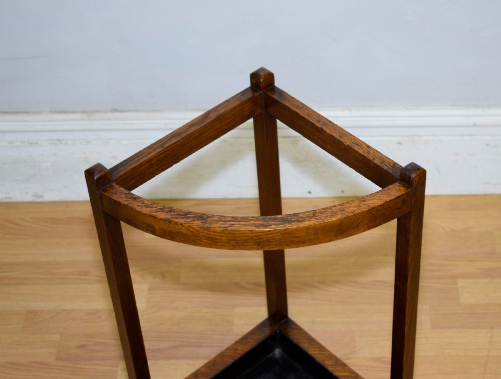 An Arts and Crafts dark oak corner stick stand featuring a curved upper front rail, straight vertical supports, and a black triangular metal drip tray. View V