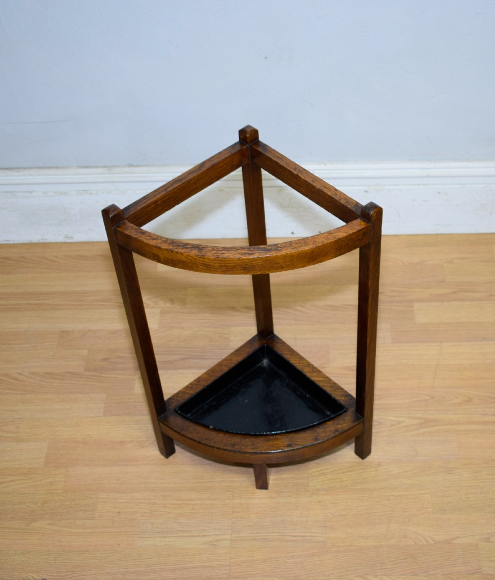 An Arts and Crafts dark oak corner stick stand featuring a curved upper front rail, straight vertical supports, and a black triangular metal drip tray. View VI