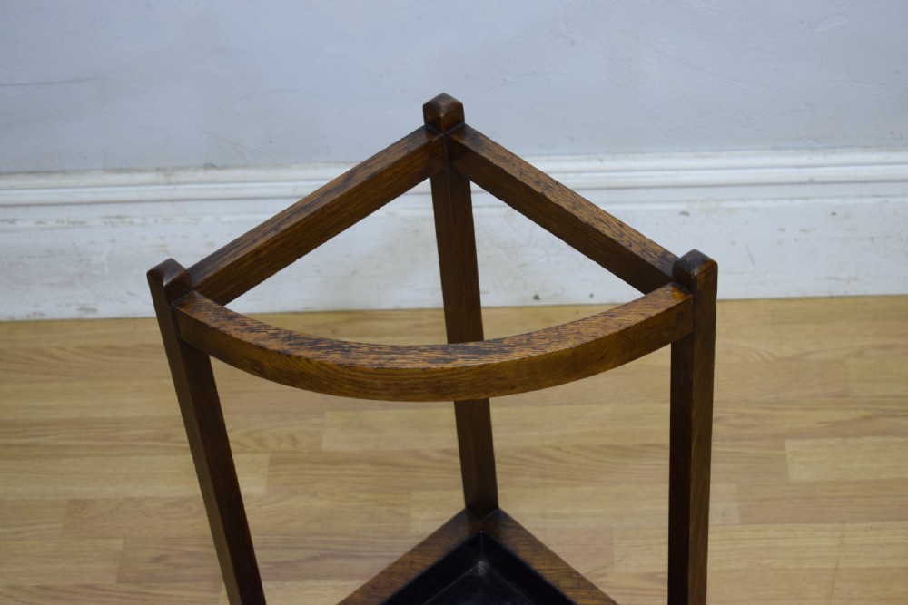 An Arts and Crafts dark oak corner stick stand featuring a curved upper front rail, straight vertical supports, and a black triangular metal drip tray. View VIII