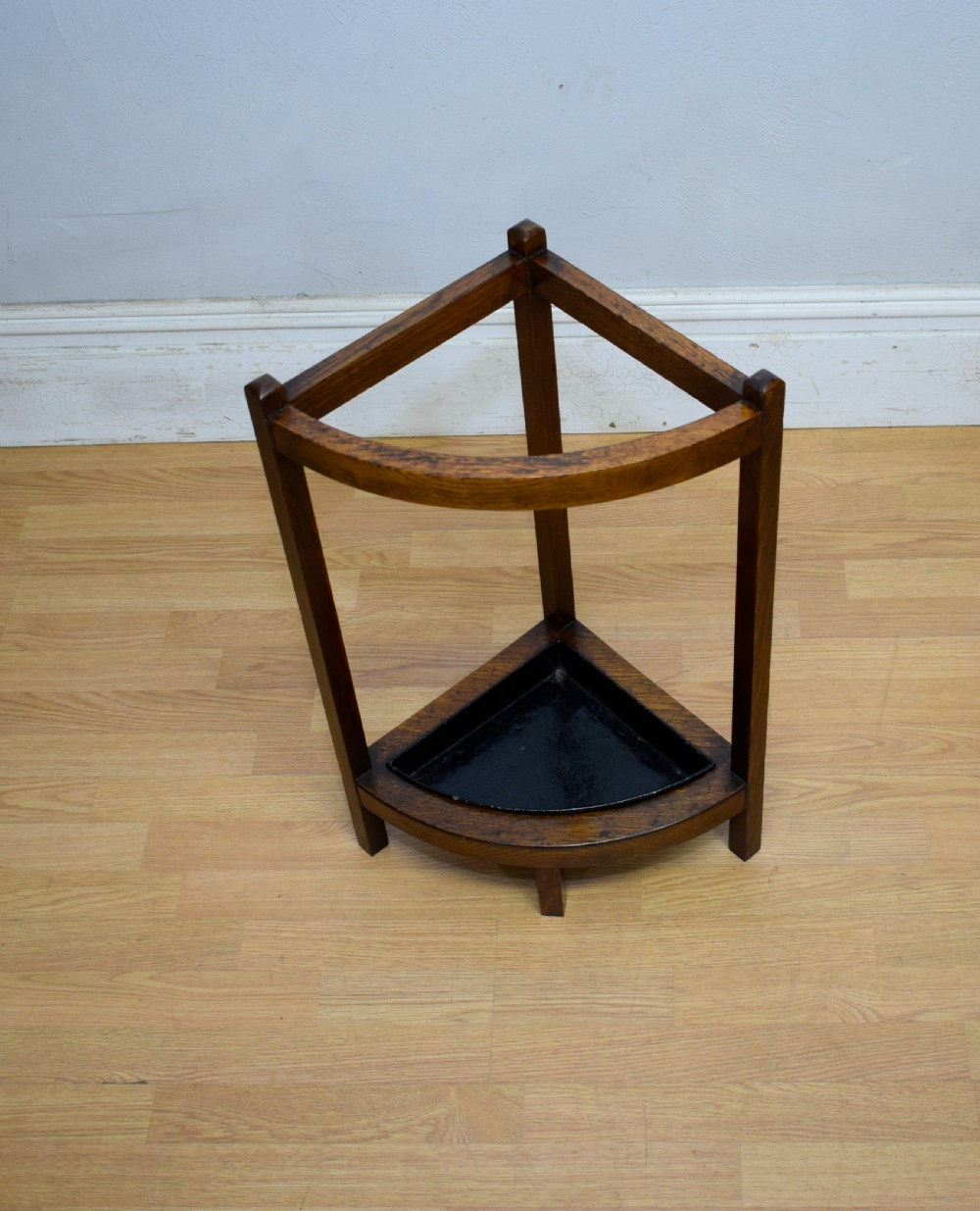 An Arts and Crafts dark oak corner stick stand featuring a curved upper front rail, straight vertical supports, and a black triangular metal drip tray. View IX