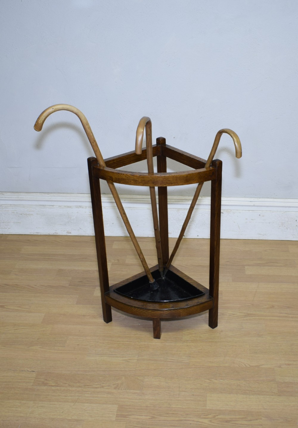 An Arts and Crafts dark oak corner stick stand featuring a curved upper front rail, straight vertical supports, and a black triangular metal drip tray.