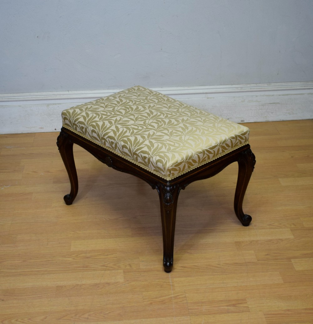 An early 20th-century French stool with carved dark timber cabriole legs and a cream and gold patterned fabric upholstered top. View II