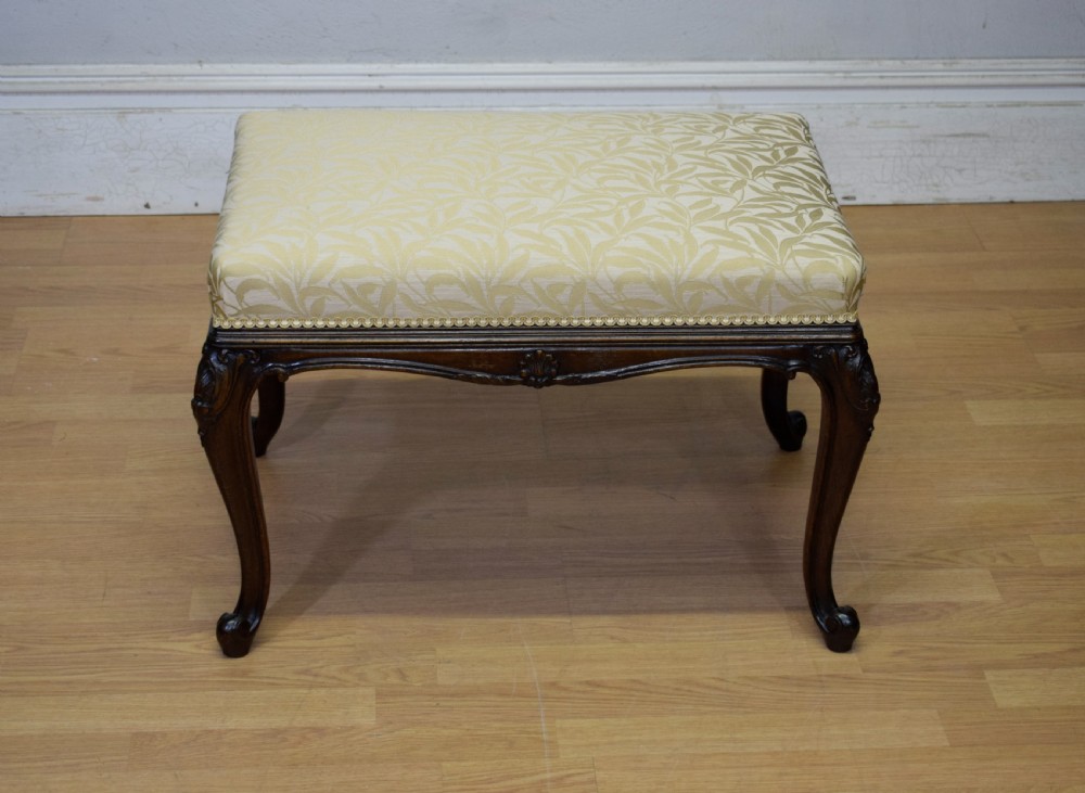 An early 20th-century French stool with carved dark timber cabriole legs and a cream and gold patterned fabric upholstered top. View IV