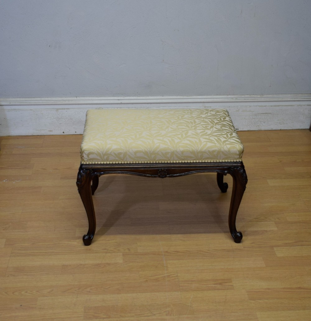 An early 20th-century French stool with carved dark timber cabriole legs and a cream and gold patterned fabric upholstered top. View V