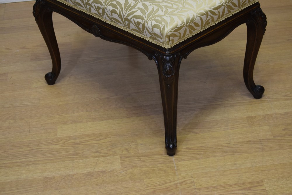 An early 20th-century French stool with carved dark timber cabriole legs and a cream and gold patterned fabric upholstered top. View VI