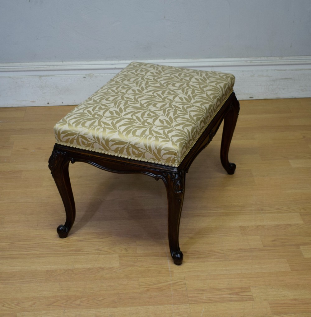 An early 20th-century French stool with carved dark timber cabriole legs and a cream and gold patterned fabric upholstered top. View VIII