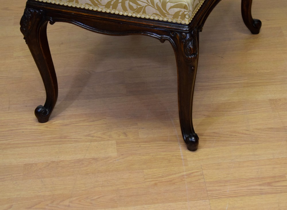 An early 20th-century French stool with carved dark timber cabriole legs and a cream and gold patterned fabric upholstered top. View IX