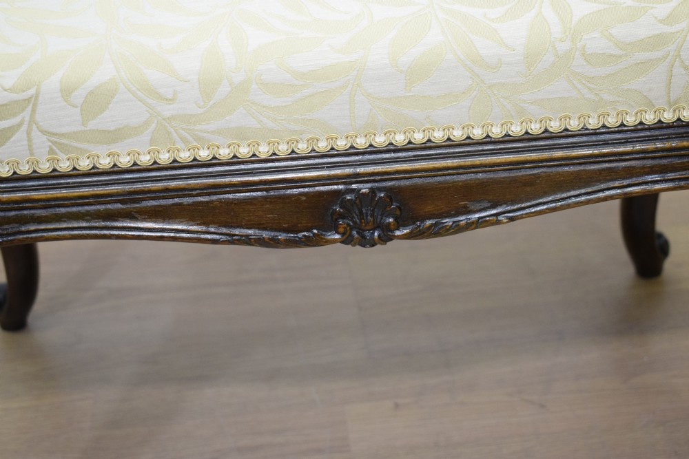 An early 20th-century French stool with carved dark timber cabriole legs and a cream and gold patterned fabric upholstered top. View XIII