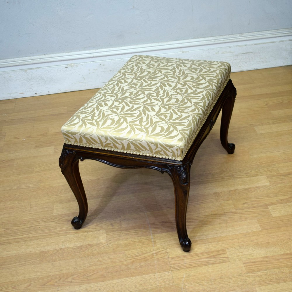 An early 20th-century French stool with carved dark timber cabriole legs and a cream and gold patterned fabric upholstered top. View XIV