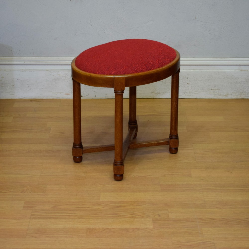 An antique Arts and Crafts oak stool featuring an oval red upholstered seat supported by four turned legs with a cross stretcher. View III