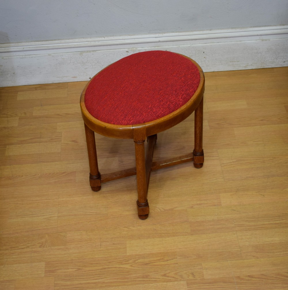 An antique Arts and Crafts oak stool featuring an oval red upholstered seat supported by four turned legs with a cross stretcher. View IV