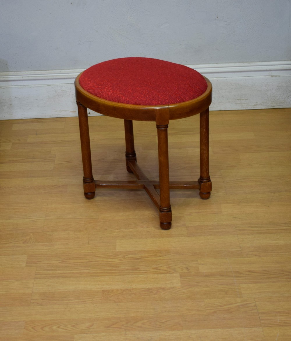An antique Arts and Crafts oak stool featuring an oval red upholstered seat supported by four turned legs with a cross stretcher. View V
