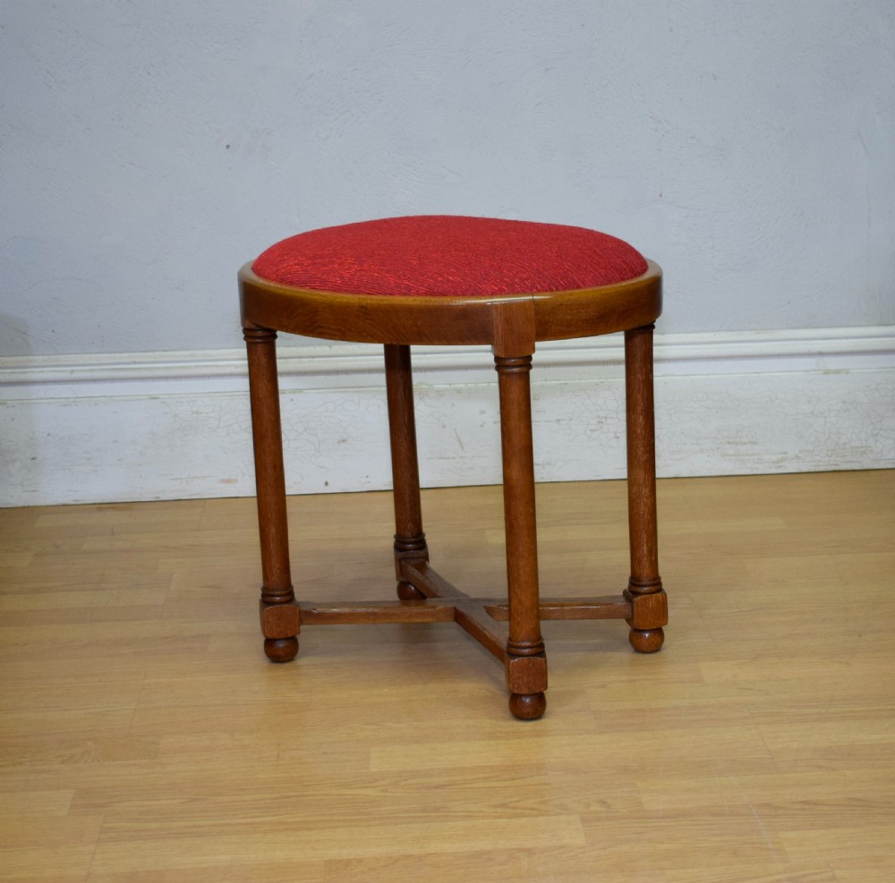 An antique Arts and Crafts oak stool featuring an oval red upholstered seat supported by four turned legs with a cross stretcher. View VI