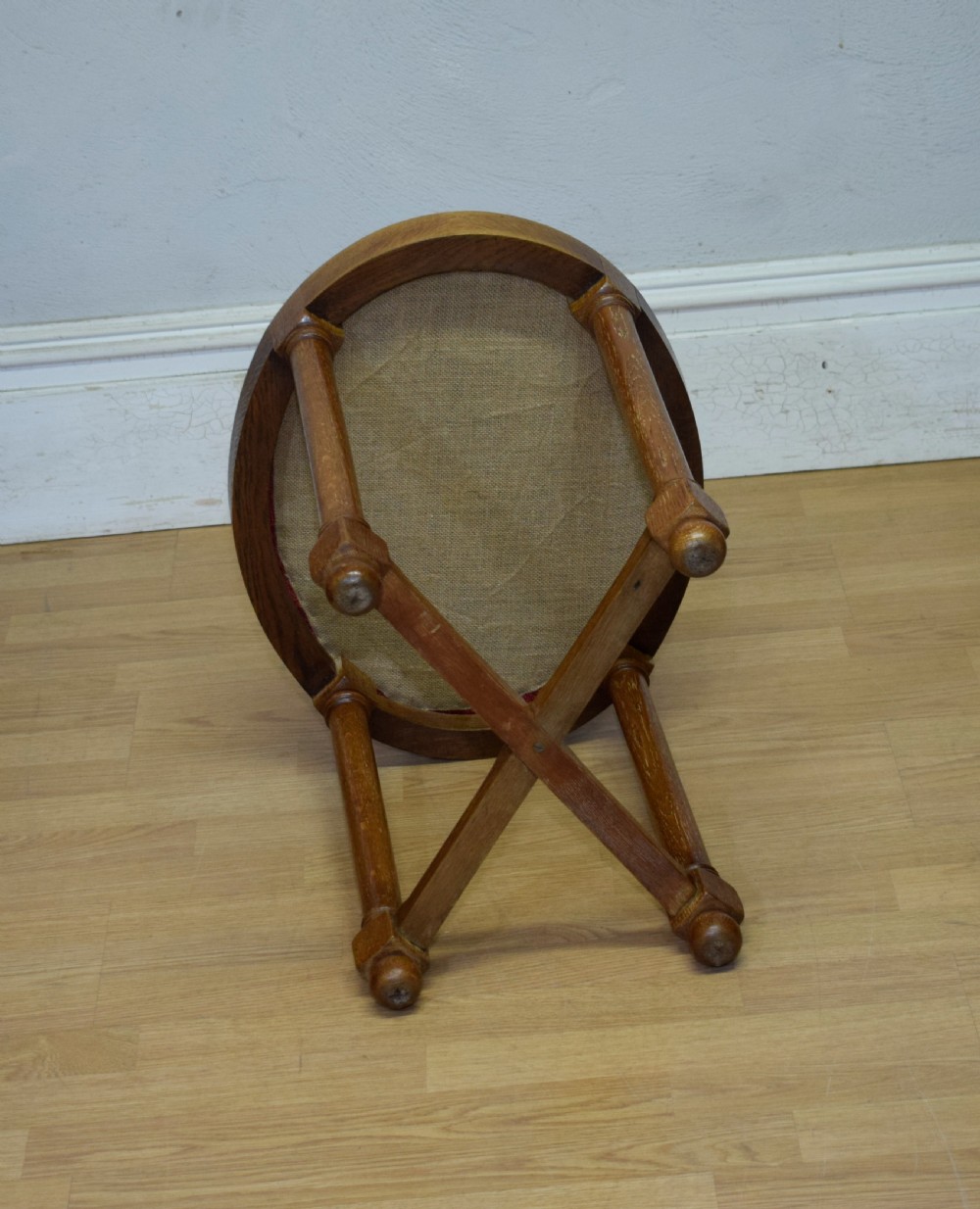 An antique Arts and Crafts oak stool featuring an oval red upholstered seat supported by four turned legs with a cross stretcher. View VIII