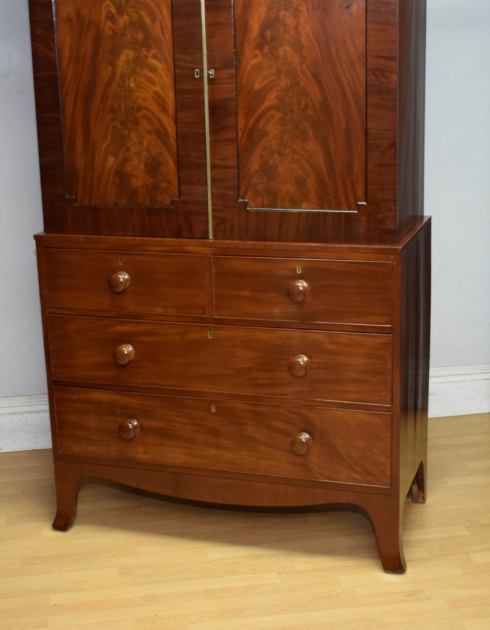 A Regency flame mahogany linen press featuring an arched pediment, twin cupboard doors above four drawers, and splayed bracket feet. View II