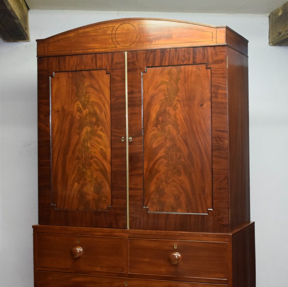 A Regency flame mahogany linen press featuring an arched pediment, twin cupboard doors above four drawers, and splayed bracket feet. View VIII