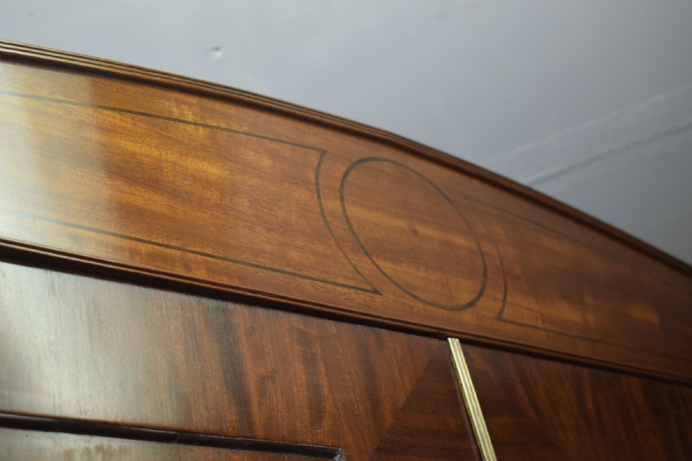 A Regency flame mahogany linen press featuring an arched pediment, twin cupboard doors above four drawers, and splayed bracket feet. View XVIII