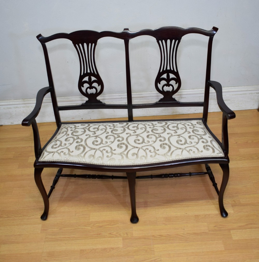 A late Victorian dark mahogany double chair-back settee featuring pierced splats, curved arms, cabriole front legs, and a patterned fabric seat.