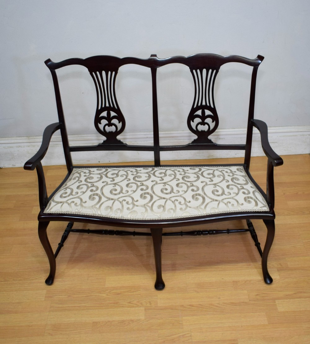 A late Victorian dark mahogany double chair-back settee featuring pierced splats, curved arms, cabriole front legs, and a patterned fabric seat. View III