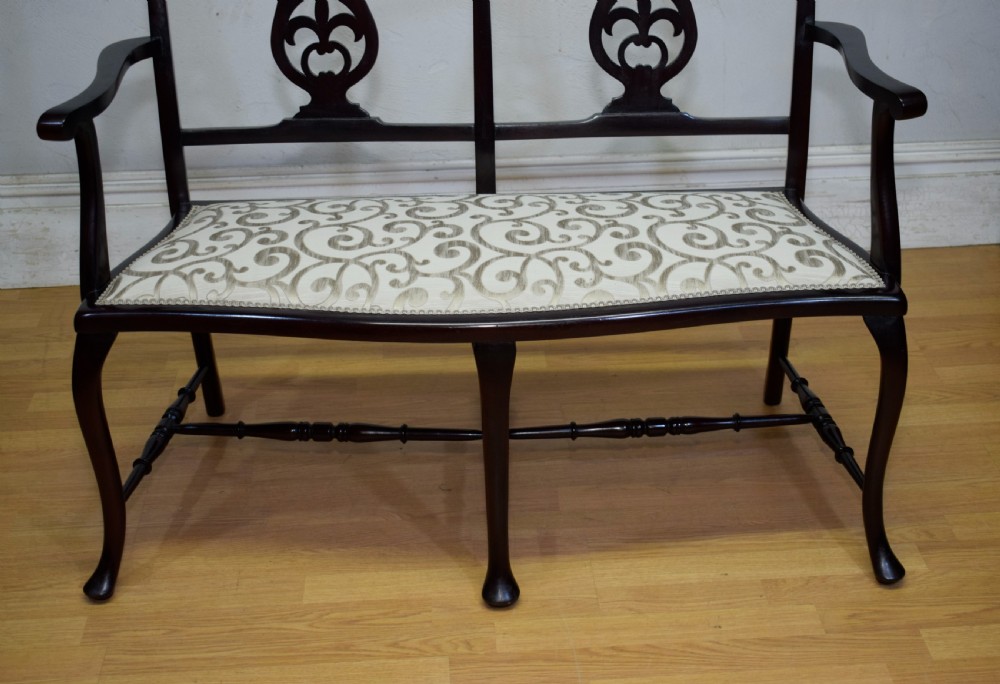 A late Victorian dark mahogany double chair-back settee featuring pierced splats, curved arms, cabriole front legs, and a patterned fabric seat. View V
