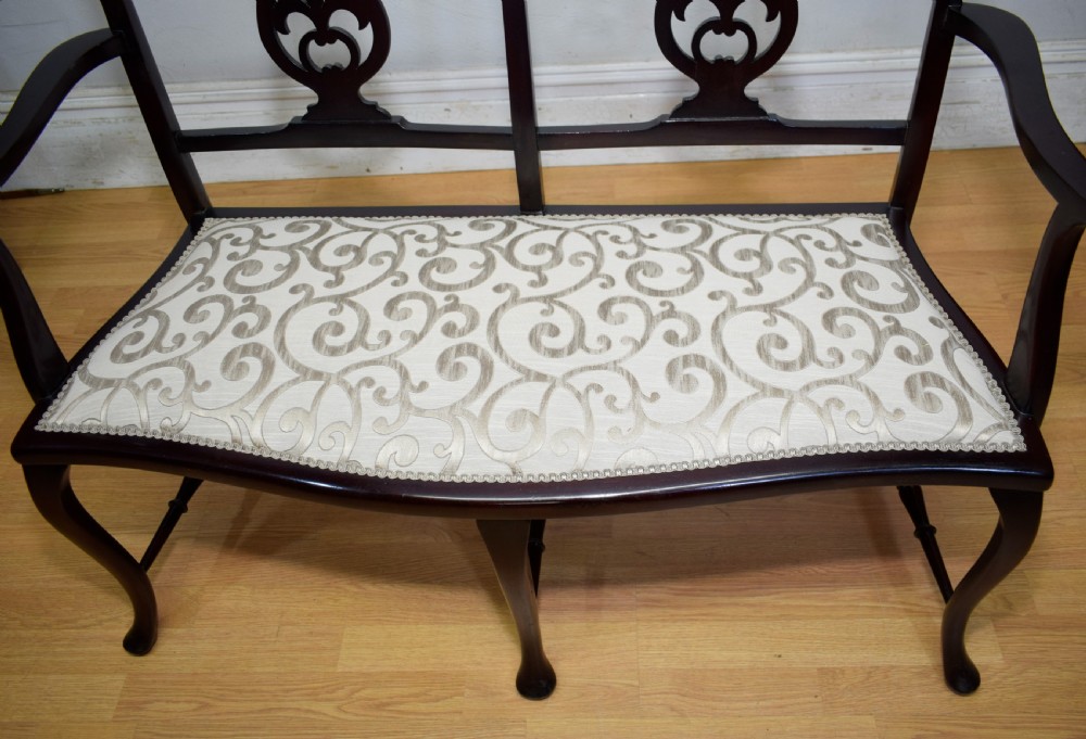 A late Victorian dark mahogany double chair-back settee featuring pierced splats, curved arms, cabriole front legs, and a patterned fabric seat. View VI