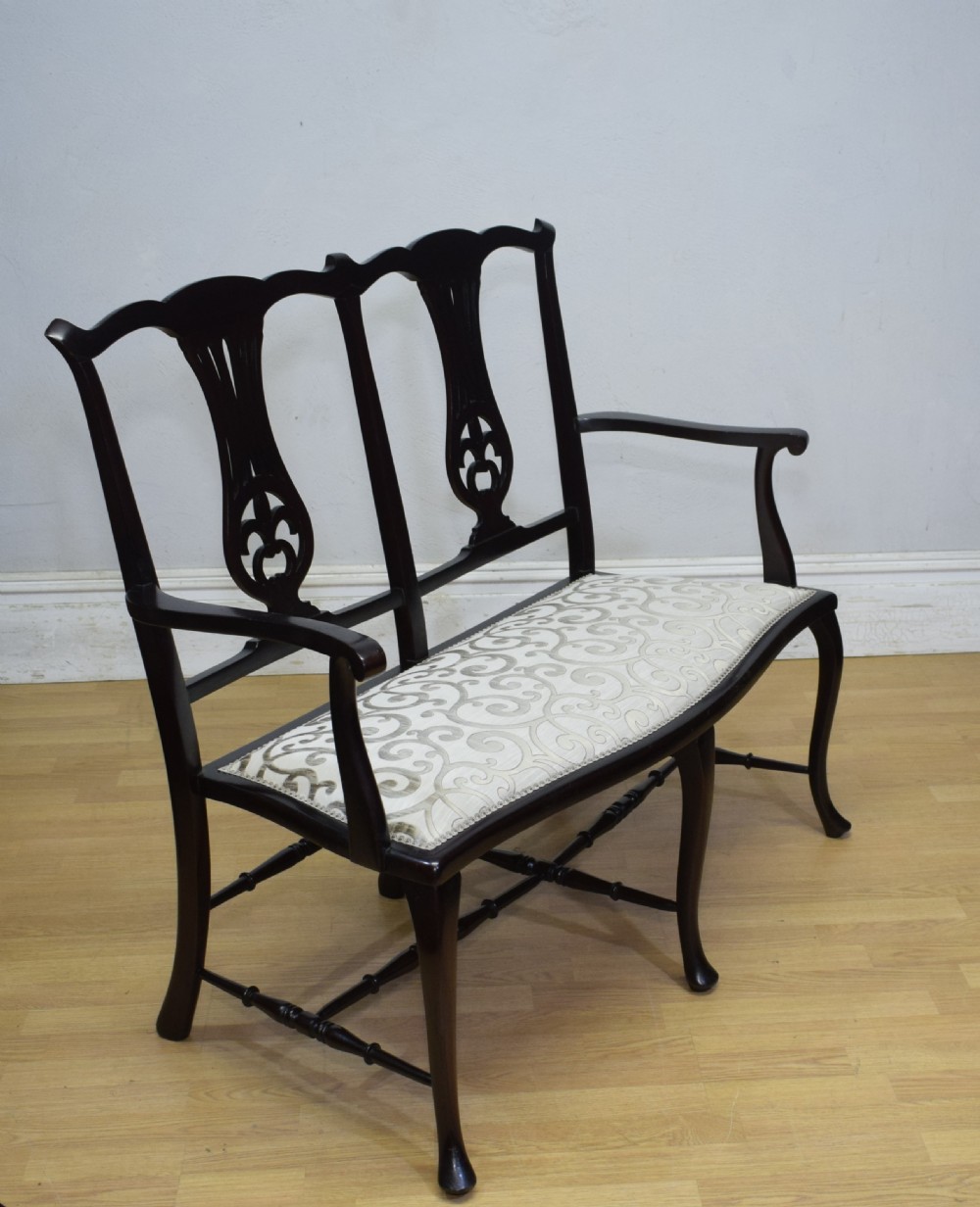 A late Victorian dark mahogany double chair-back settee featuring pierced splats, curved arms, cabriole front legs, and a patterned fabric seat. View IX