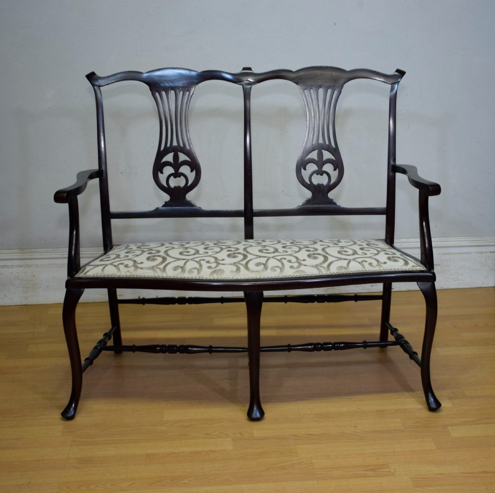 A late Victorian dark mahogany double chair-back settee featuring pierced splats, curved arms, cabriole front legs, and a patterned fabric seat. View X
