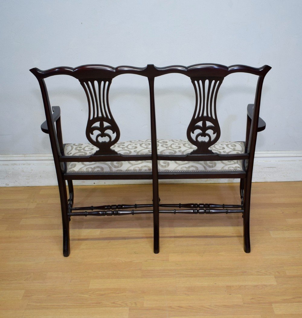 A late Victorian dark mahogany double chair-back settee featuring pierced splats, curved arms, cabriole front legs, and a patterned fabric seat. View XIV