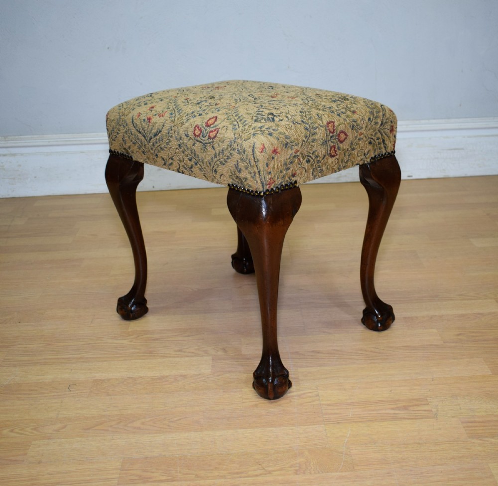A square Chippendale style stool upholstered in floral patterned fabric with dark mahogany cabriole legs and claw-and-ball feet.