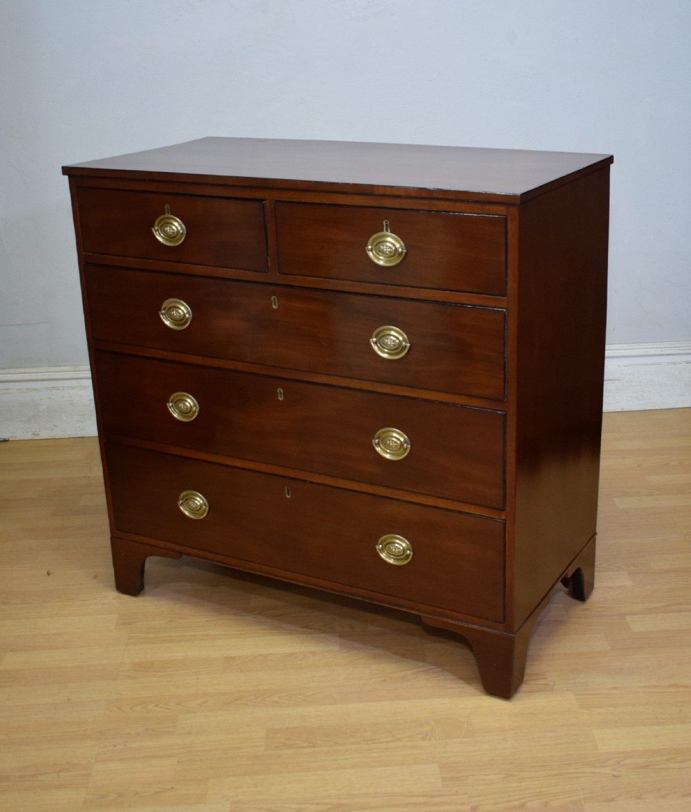 A Regency period mahogany chest of drawers featuring a two short over three long graduated drawer layout with polished brass oval handles and bracket feet. View II