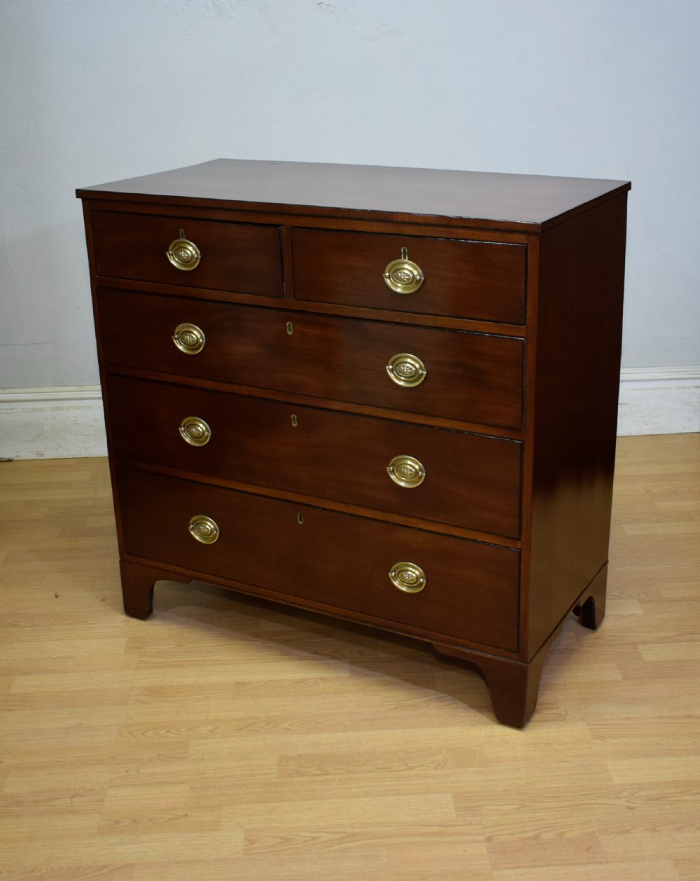 A Regency period mahogany chest of drawers featuring a two short over three long graduated drawer layout with polished brass oval handles and bracket feet. View III