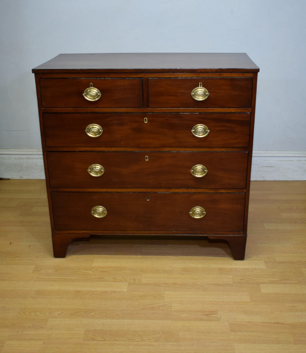 A Regency period mahogany chest of drawers featuring a two short over three long graduated drawer layout with polished brass oval handles and bracket feet. View V