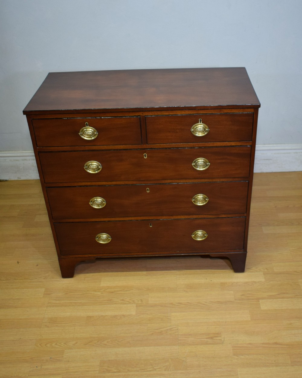 A Regency period mahogany chest of drawers featuring a two short over three long graduated drawer layout with polished brass oval handles and bracket feet. View VI