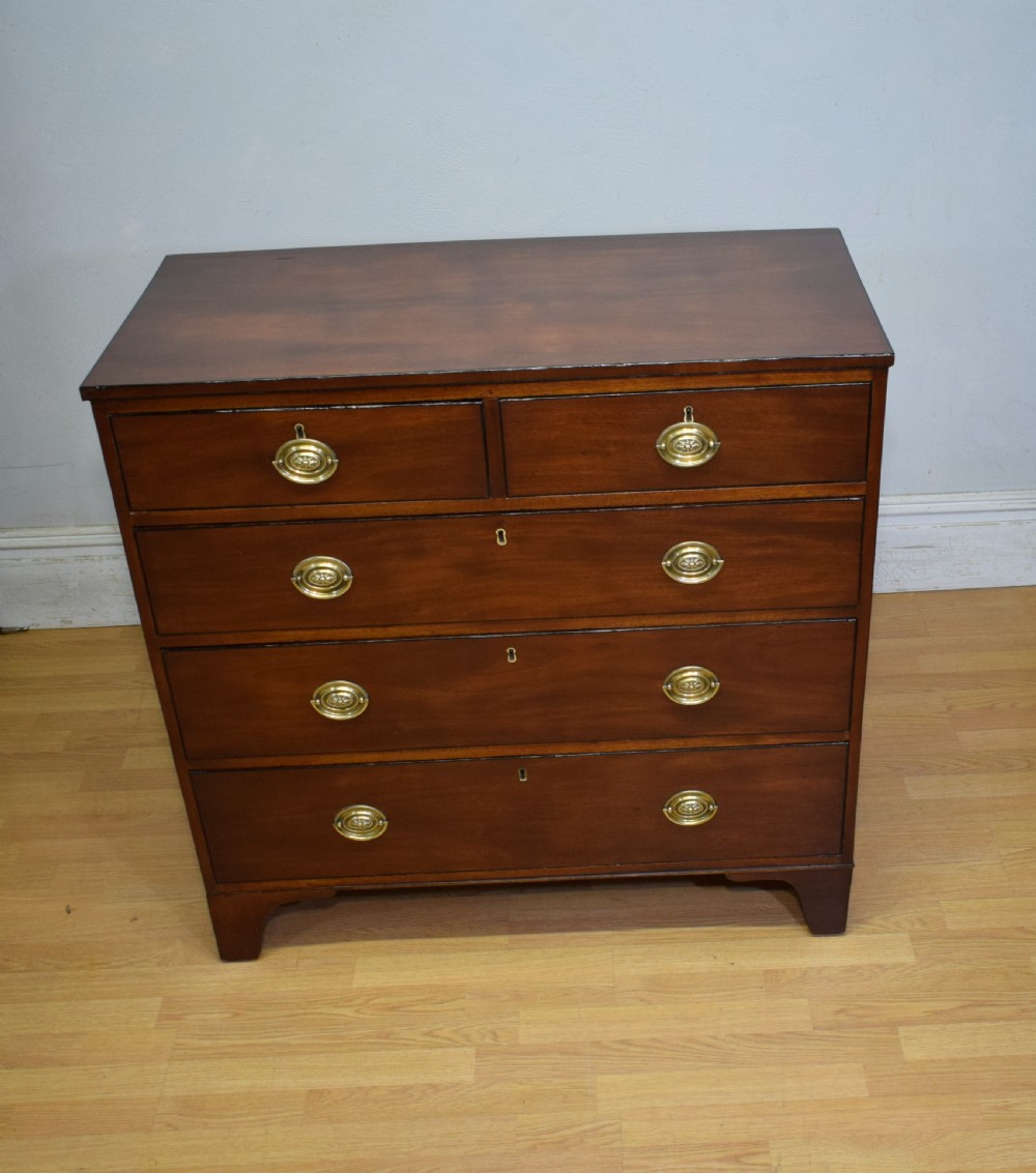 A Regency period mahogany chest of drawers featuring a two short over three long graduated drawer layout with polished brass oval handles and bracket feet. View VII