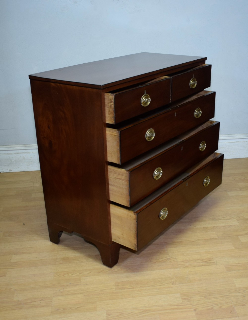 A Regency period mahogany chest of drawers featuring a two short over three long graduated drawer layout with polished brass oval handles and bracket feet. View IX