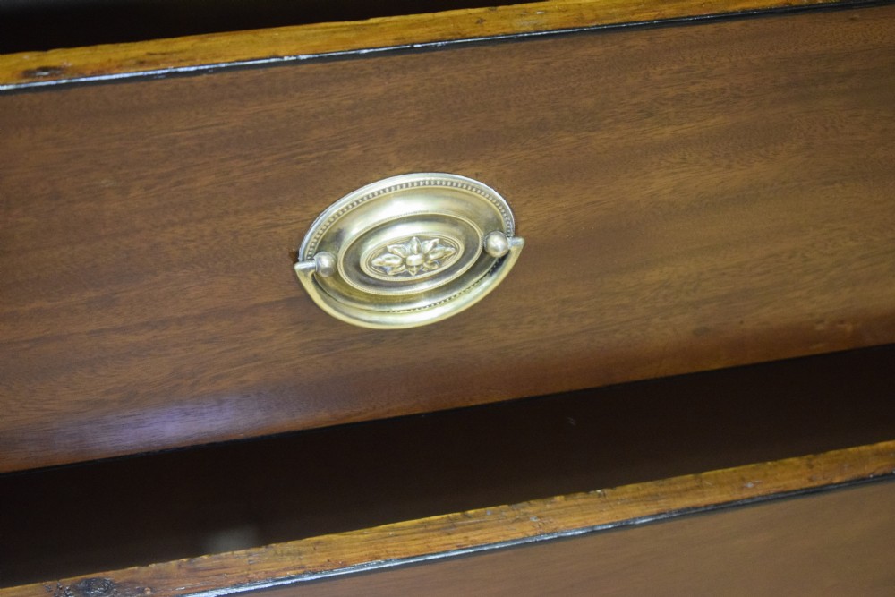 A Regency period mahogany chest of drawers featuring a two short over three long graduated drawer layout with polished brass oval handles and bracket feet. View X
