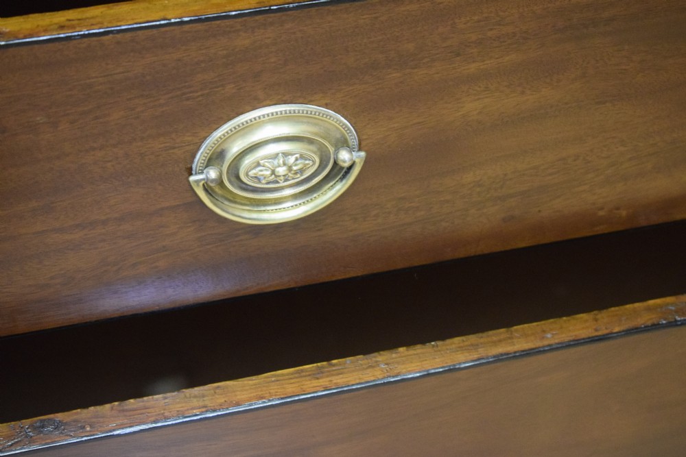 A Regency period mahogany chest of drawers featuring a two short over three long graduated drawer layout with polished brass oval handles and bracket feet. View XI