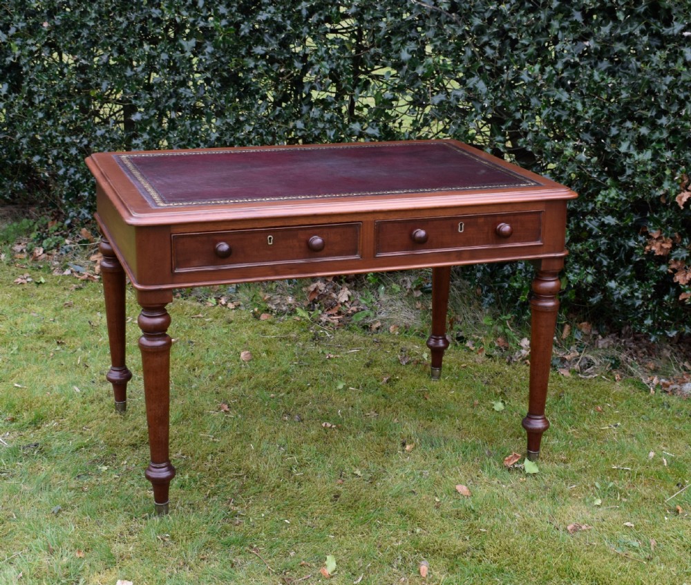 A Victorian mahogany writing table featuring a dark red leather insert top, two frieze drawers with wooden knobs, and four turned legs.